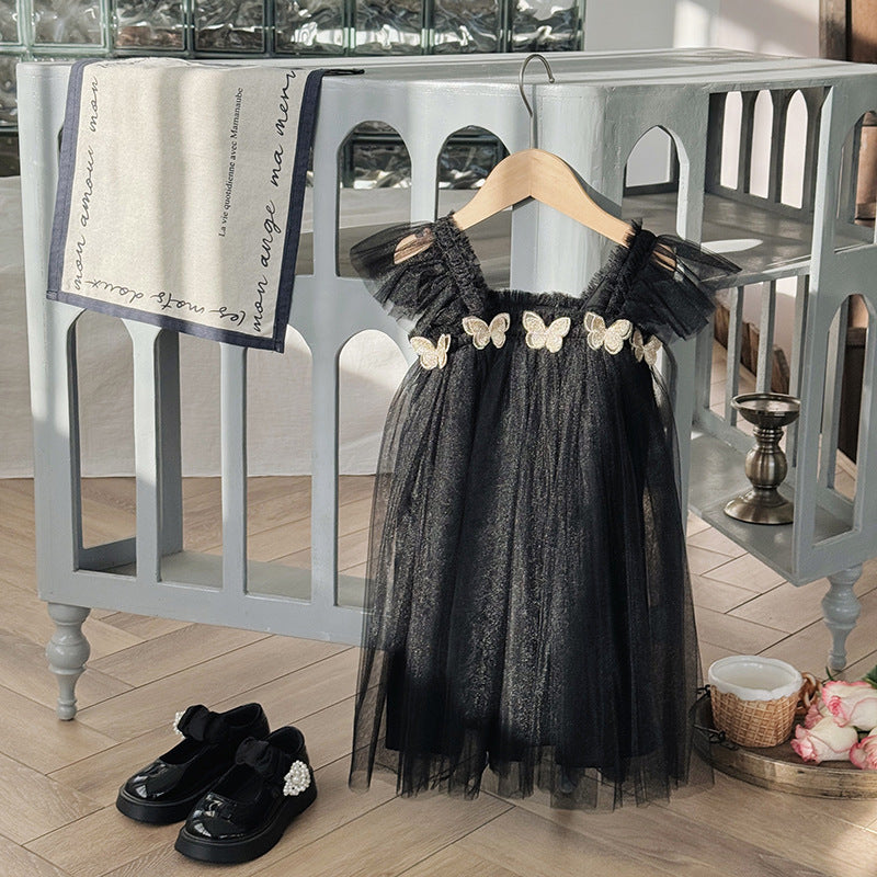 Black dress with butterfly embellishments on a hanger in a room setting.